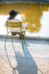 Wall Mural - Woman in hat sitting back on the famous green chair near the fountain in Tuileries park during the morning light in Paris