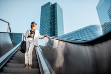 Stylish Businesswoman In White Suit Going Down On The Escalator At The Business Centre Outdoors With Skyscrapers On The Background In Paris
