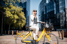 Portrait Of A Stylish Business Woman In White Suit Standing With Bicycle At The Financial District With Modern Buildings On The Background