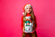 © Shopping King Louie - Teenage girl wearing Santa hat and tinsel on neck holding Christmas gift boxes, on red background. Christmas gifts concept