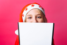 Girl In Santa Hat And Tinsel On The Neck, A Teenager Holding A Tablet With A Blank Sheet, Making Plans For The New Year On A Red Background