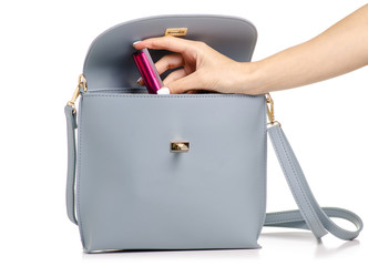 Wall Mural - A hand put cosmetic lipsticklip gloss in the female blue gray leather handbag on a white background isolation