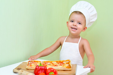 A little boy baker and pizza maker in a white chef's cap and apron is smiling because he cooked delicious and beautiful puff pastry pizza.
