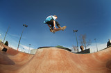 Low angle view of man jumping with skateboard at skate ramp against blue sky