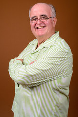 Overweight senior man wearing eyeglasses against brown backgroun