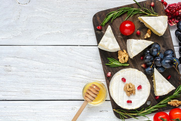 Wall Mural - camembert cheese with grapes, tomatoes cherry, pomegranate seeds, walnuts and rosemary on wooden cutting board