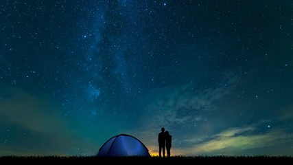 Wall Mural - The couple near a camping tent standing on the starry sky background. time lapse
