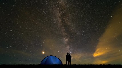Wall Mural - The couple near a camping tent standing on a meteor shower background