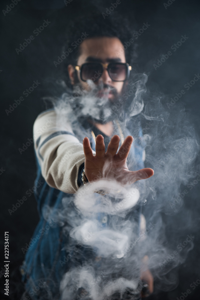 Smoking vape. vaping man holding a mod. Vape Rings. A man launches a ring  of smoke. Tricks with smoke. Stock Photo