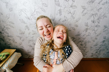 Young mother with child beautiful girl crying and laughing together. Wide angle funny portrait of woman holding her little .crying daughter. Family pair emotional face expressions at home. Poor baby.