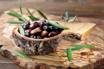 Wall Mural - Fresh brown kalamata olives and olive tree leaves in authentic greek wooden bowl with bark, close up view