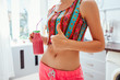 Woman drinking a homemade fruity detox smoothie wearing sportive clothing on kitchen