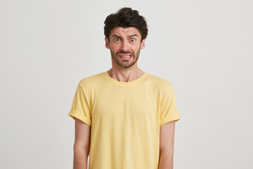 Indoor photo of afraid fearful young man with dark brown hair and beard wears yellow casual tshirt, isolated over white background