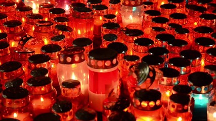 Wall Mural - A lot of Illuminated Votive candles glows on a grave at night. Burning candles lantern on cemetery. All saints day. Prayer candles in a Catholic church.