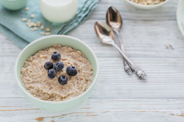 Oatmeal porridge bowl on the white wooden background.