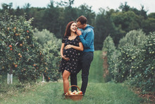 Happy Healthy Pregnancy And Parenting. Portrait Of Pregnant Young Brunette Caucasian Woman With Husband On Apple Farm. Beautiful Expecting Mother And Future Father At Countryside, Rustic Style