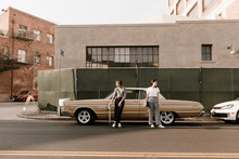 Two Young Stylish Women Standing Together In Front Of Vintage Car