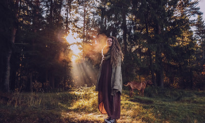 Young woman with dreadlocks in autumn fall forest in the morning sunshine