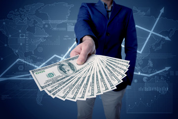 Young businessman holding large amount of bills with blue charts in the background