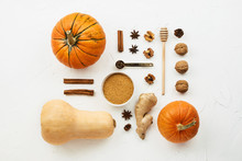 Flat Lay With Various Pumpkins, Cinnamon Stick And  Cane Sugar Knolled Together On White Cement Background