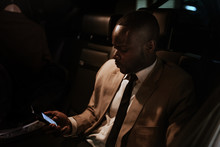 Black Businessman Inside The Car Looking At His Mobile Phone