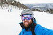 © blurMEDIA/Stocksy - Bearded man pauses to take a selfie while skiing down a mountain