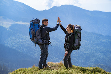 Wall Mural - the happy couple with backpacks standing on the mountain landscape background