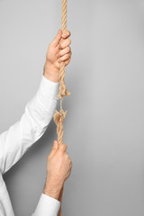 Wall Mural - Man climbing frayed rope on gray background