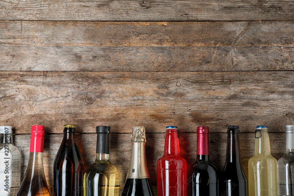 Bottles with different alcoholic drinks on wooden background, top view. Space for text - obrazy, fototapety, plakaty 