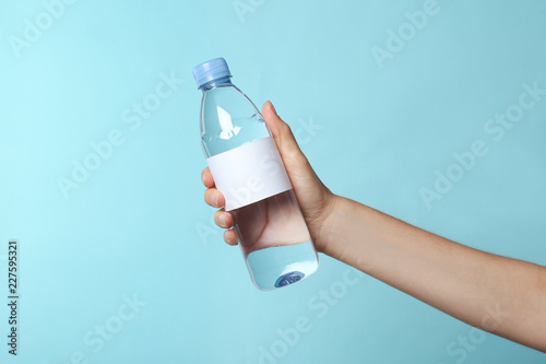 Woman holding plastic bottle of pure water with blank tag on color background Wallpaper Mural
