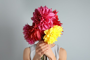 Woman holding bouquet of beautiful dahlia flowers against gray background