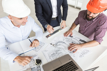 male engineers, architects working at the desk in helmets. Drawings, laptop, roulette on the desktop. Reception and supervision of building construction