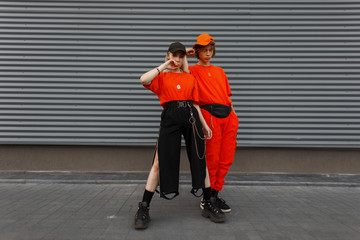 Beautiful young stylish woman with a handsome young man in fashionable orange stylish clothes with caps posing near the gray metal wall. Fashion couple