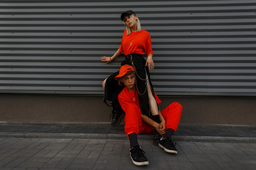 Stylish beautiful young fashion couple in bright fashionable orange clothes near the metal wall on the street