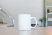 White Mug On Table And Modern Room Background. Blank Drink Cup For Your Design. Can Put Text, Image, And Logo.