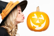 Sensual Halloween Witch Kissing Jack O' Lantern. Attractive Young Woman Dressed In Witch Halloween Costume And Large Halloween Pumpkin Isolated Over White Background.