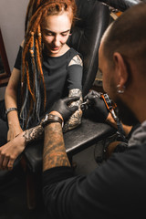 Wall Mural - girl with dreadlocks in a tattoo parlor. The master creates a picture on the body of a young beautiful girl. Close-up of hands and tattoo machine