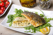 Grilled seabass fillet with arugula, lemon, tomatoes and capers. Close-up.