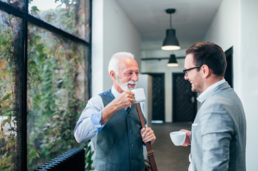 Smiling senior and young business men on a coffee break.