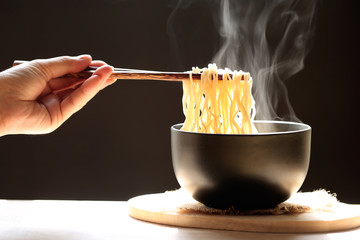 Woman hand holding chopsticks of instant noodles in cup with smoke rising dark background, Sodium diet high risk kidney failure, Healthy eating concept