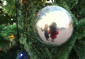 Reflection of two human figures in the Christmas ball on the branches of artificial fir