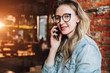 © foxyburrow - Young businesswoman has telephone conversations.Cheerful girl blogger in trendy glasses sitting in cafe,talking on phone