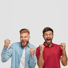 Photo of successful men raise fists, tell yes, feel joyful and proud of themselves, have happy expressions, celebrate something, stand against white background with free space for text or promotion