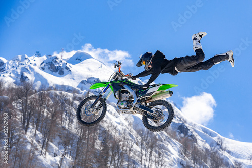 Fototapety Wyścigi Motocyklowe  zawodnik-na-motocyklu-w-locie-skacze-i-startuje-na-trampolinie-na-tle-snieznego-mo