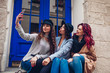 © maryviolet - Three beautiful women taking selfie on city street. Friends hanging and having fun