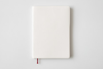 top view of closed blank white leather cover notebook on white desk background with copy space