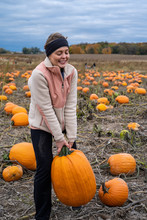 Adult Woman (30s) Attempts And Struggles To Lift And To Pick Up A Giant Pumpkin From A Pumpkin Patch. Smiling And Laughing And Having Fun