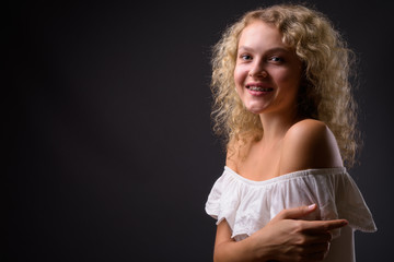 Young beautiful woman with blond curly hair against gray backgro