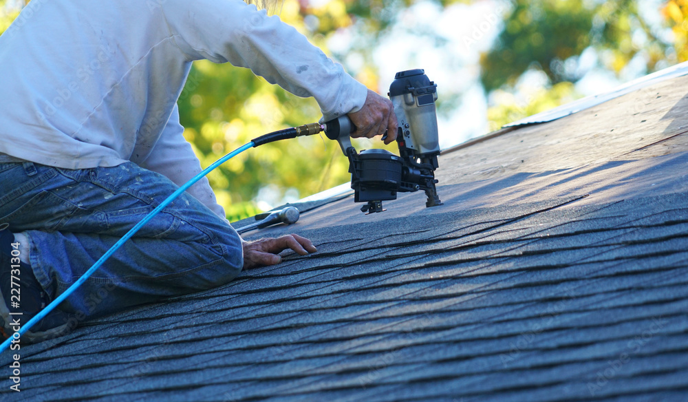 handyman using nail gun to install shingle to repair roof - obrazy, fototapety, plakaty 