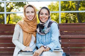 Poster - Photo of two islamic women wearing headscarfs, sitting in green park and reading book